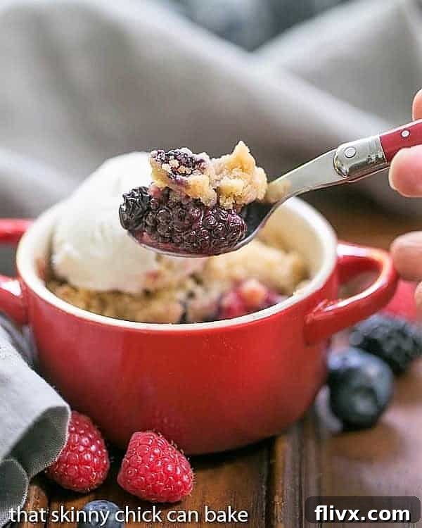 A spoon with a small scoop removed from an Individual Berry Crisp, showing the juicy berry filling and crispy topping.