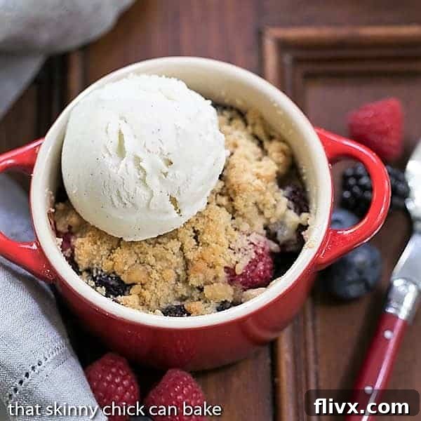 overhead view of a berry crisp with a scoop of vanilla ice cream in a small red ramekin