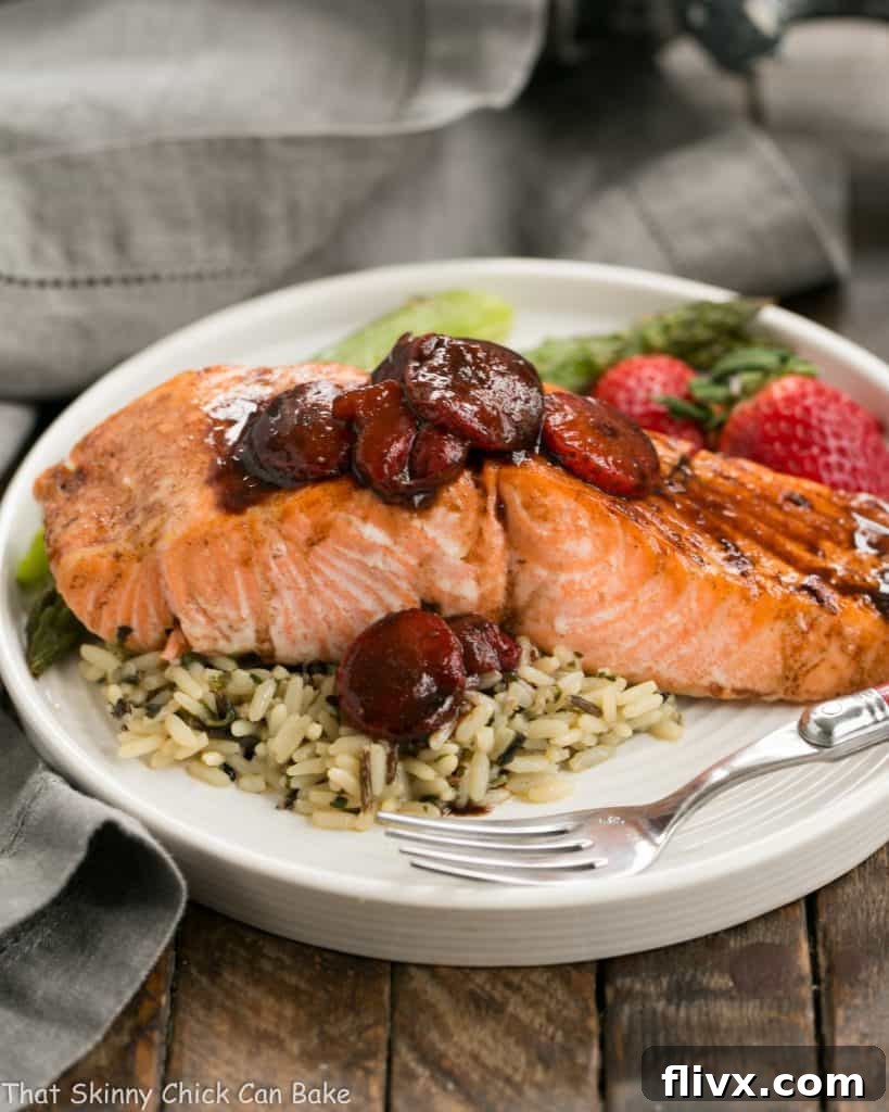 Strawberry Glazed Salmon served on a white dinner plate with fluffy white rice and fresh strawberry slices, garnished with a sprig of herb.