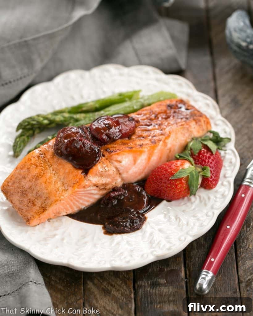 Strawberry Glazed Salmon served on a dinner plate alongside steamed green asparagus spears and fresh strawberry halves, adorned with herbs.