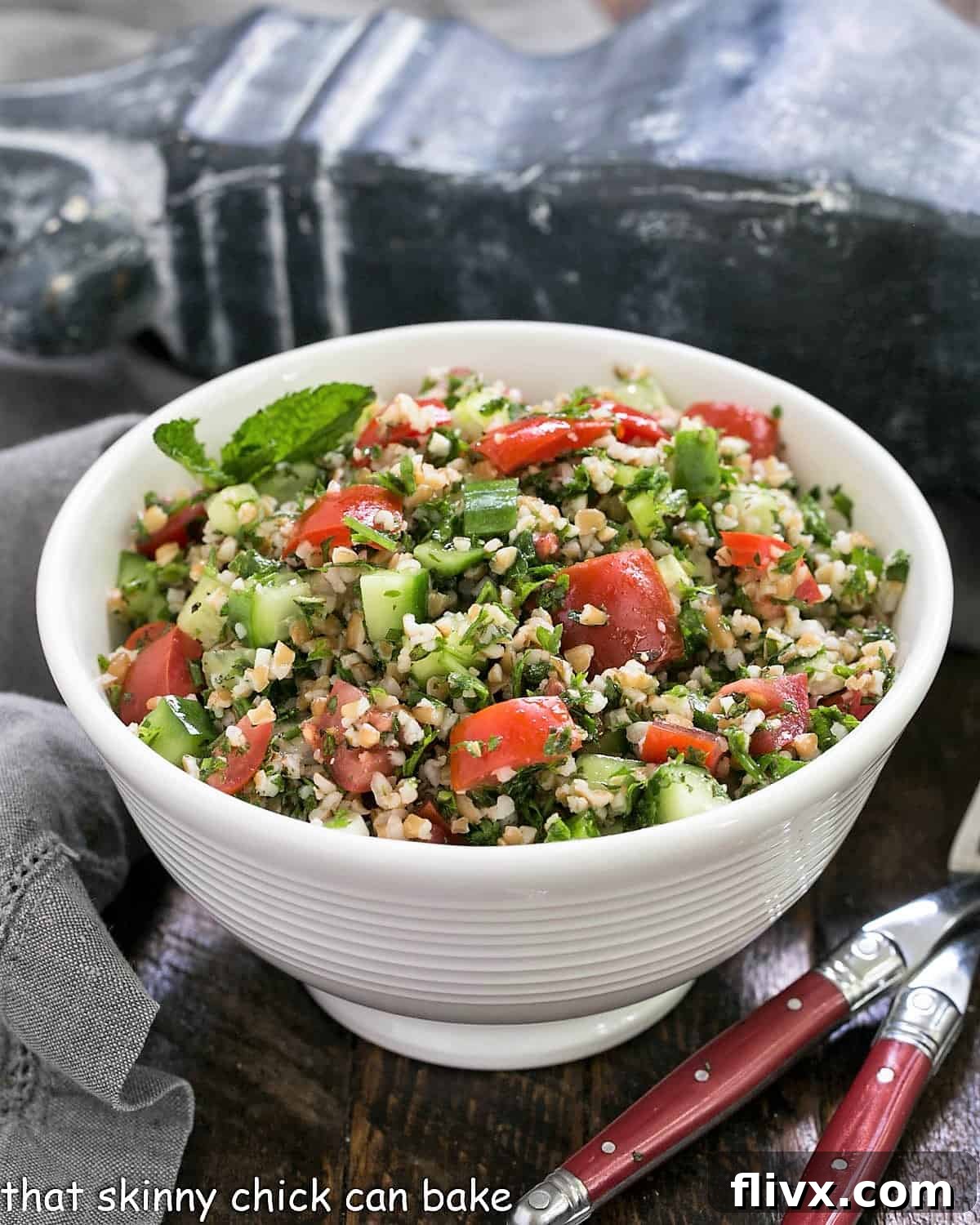A taboouli recipe in a white serving bowl with 2 forks.