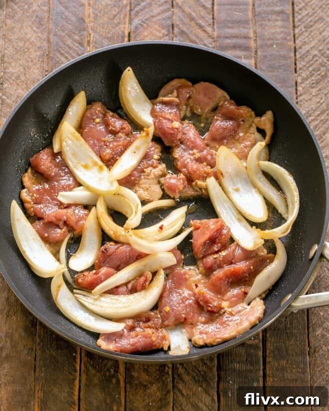 Marinated pork and onions sizzling in a hot skillet, halfway through cooking.