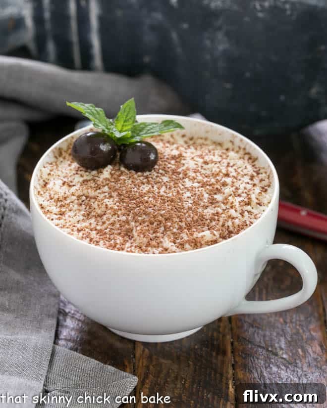 A teacup filled with chocolate tiramisu garnished with cocoa and espresso beans and a sprig of mint