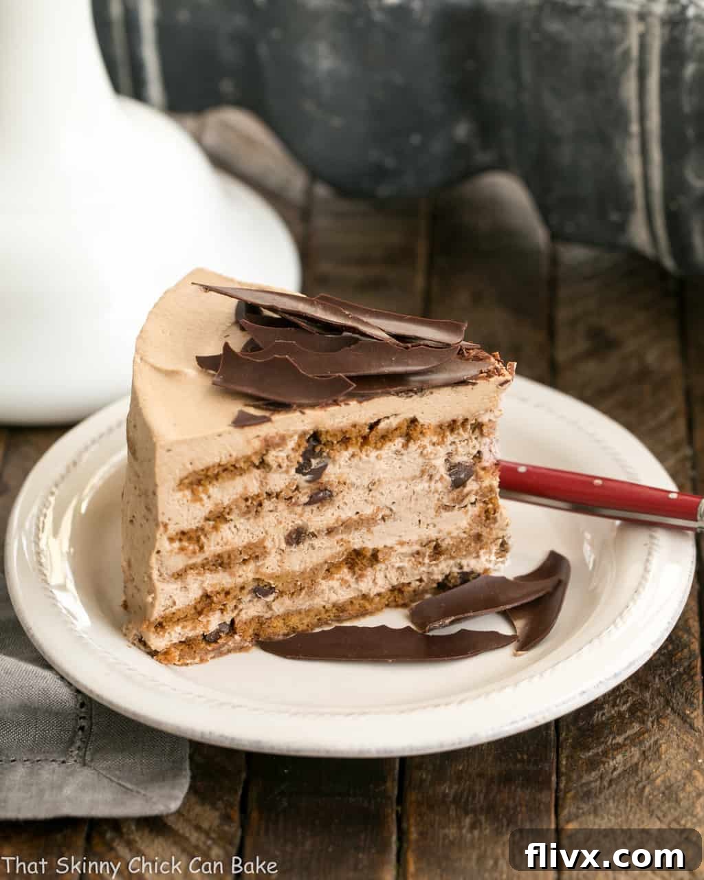 A close-up of a delectable slice of No-Bake Mocha Chocolate Chip Cookie Icebox Cake, garnished elegantly with delicate chocolate shards on a white plate, highlighting its rich layers.
