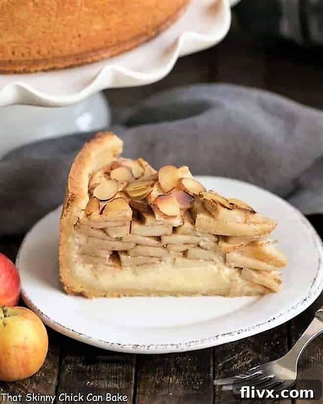 A slice of Cream Cheese Apple Torte on a white dessert plate, with a background featuring a cake stand and fresh apples.