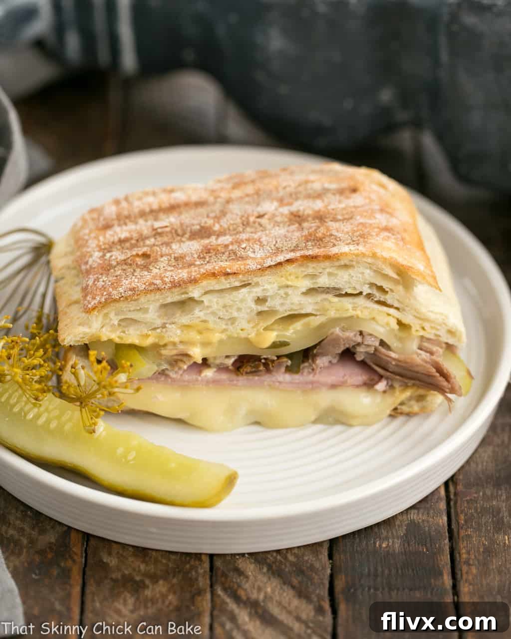 Ciabatta Cubano Sandwich Recipe on a round plate with a dill pickle, showcasing its perfectly pressed exterior and delicious layers.