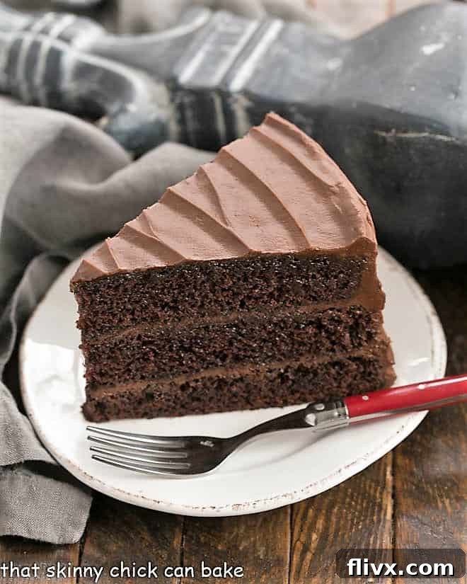 A slice of Hershey's Chocolate Cake on a white dessert plate with a vibrant red fork, ready to be enjoyed.