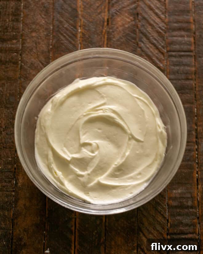 A mixing bowl with cream cheese and marshmallow creme being blended together using an electric mixer to create a smooth, creamy base for the s'mores dip.