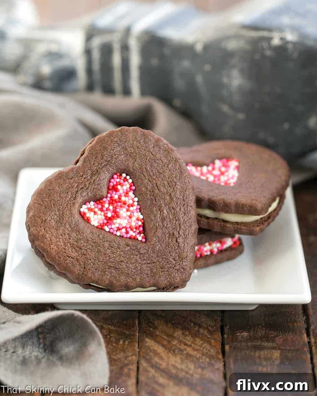Close-up of Chocolate Heart Sandwich Cookies on a square white plate, showing the detailed cut-out and sprinkles.