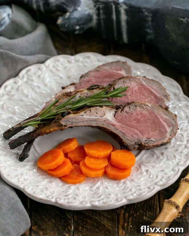 Overhead view of grilled lamb chops on a white decorative plate with a sprig of rosemary and carrot coins, highlighting the golden-brown crust.