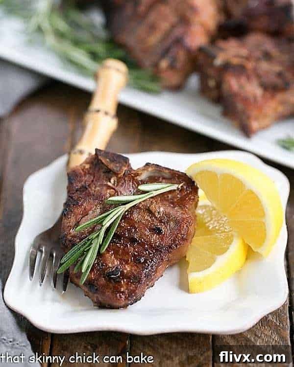 Close-up of perfectly grilled lamb chops with a vibrant sprig of rosemary and lemon wedges on a small white plate, ready to be enjoyed.