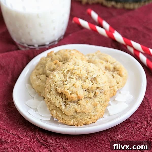 A stack of perfectly baked Chewy Coconut Cookies on a white plate, accompanied by a tall glass of milk with two straws, set against a rustic background, inviting a delightful snack time.