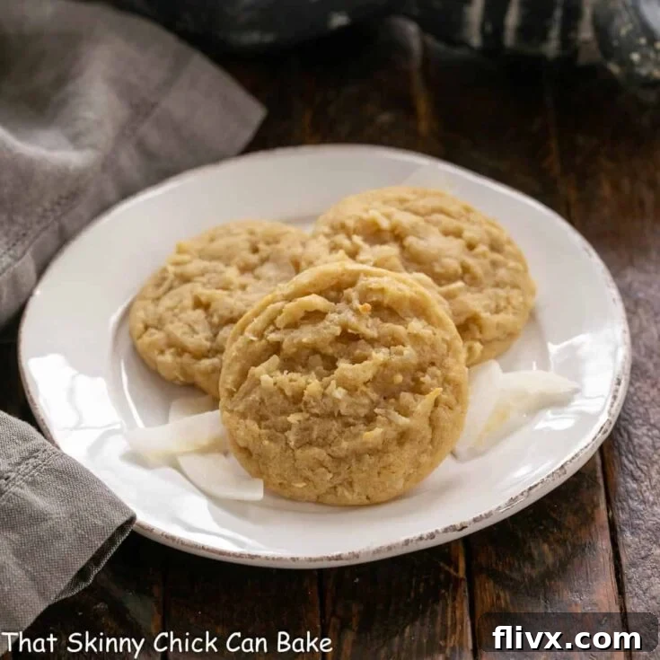 Three golden-brown chewy coconut cookies arranged invitingly on a white ceramic plate, ready to be served. A glass of milk sits nearby.