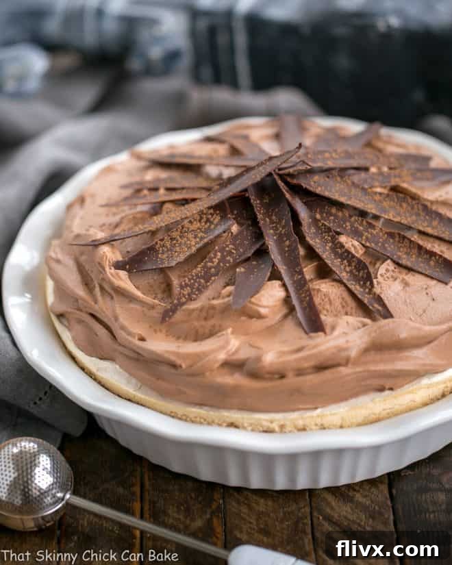 Chocolate Velvet Pie with Meringue Crust in white pie plate topped with chocolate shards and dusted with cocoa powder, ready to be served.