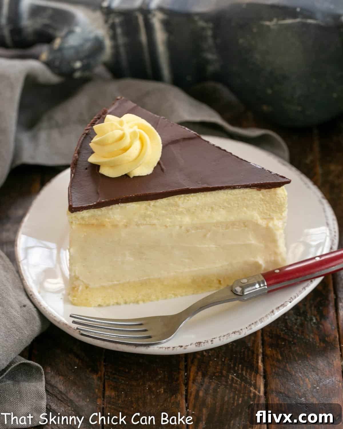 A perfectly sliced piece of Boston Cream Pie Cheesecake on a white dessert plate, showing all the distinct layers.