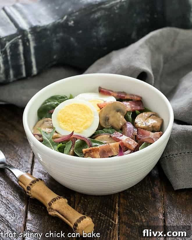Salad bowl with a spinach bacon salad with a bamboo handle fork. The salad is vibrant with green spinach, red onion, white egg slices, and golden brown bacon pieces.