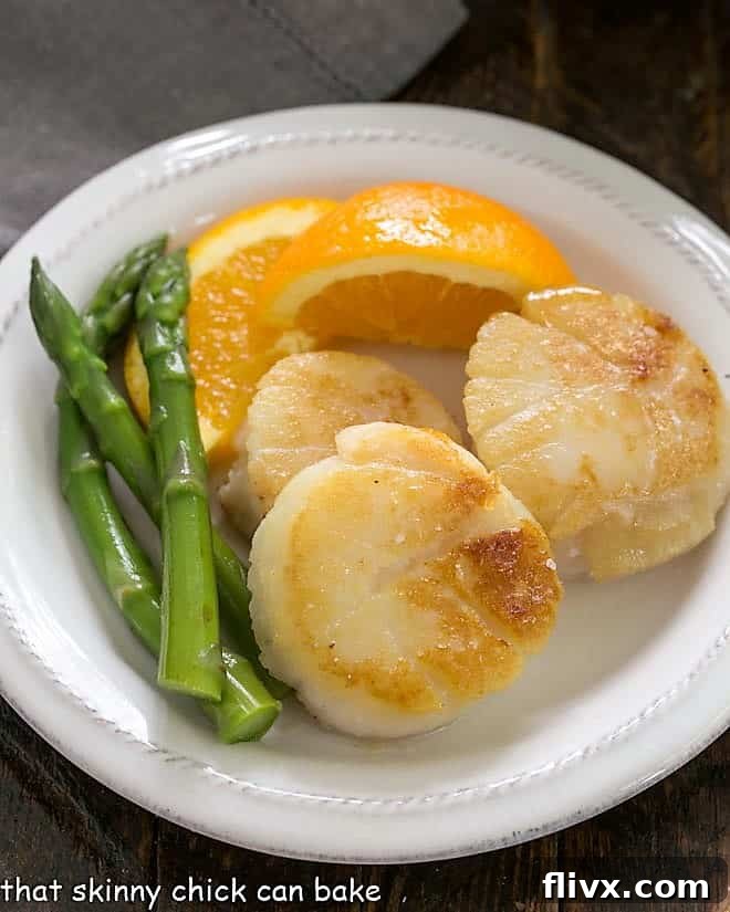 Scallops, asparagus and orange wedge on a white ceramic plate, beautifully arranged.