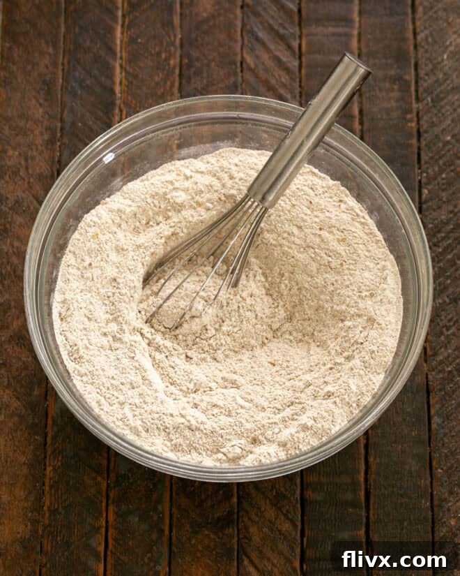Dry ingredients for Irish Brown Bread, including flours, oats, sugar, salt, and baking soda, being whisked together in a large mixing bowl.