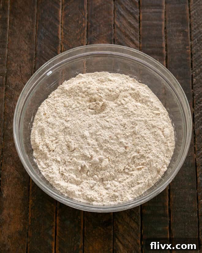 Cold butter pieces being rubbed into the dry ingredient mixture with fingertips until it resembles coarse cornmeal.