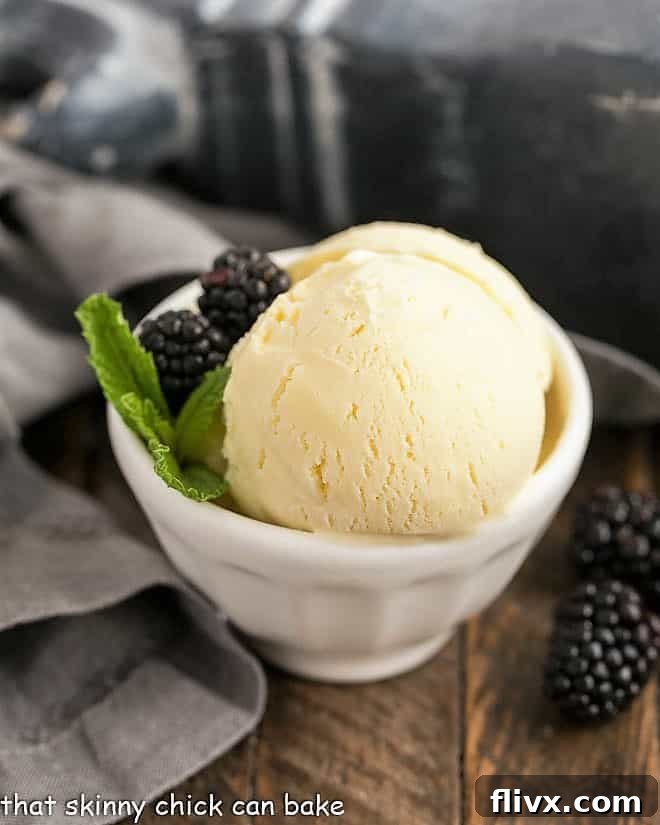 A scoop of homemade White Chocolate Ice Cream in a white bowl, garnished with fresh blackberries and a sprig of mint, highlighting its rich, creamy texture.