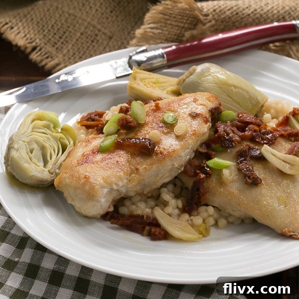 Golden brown chicken with artichokes and sun-dried tomatoes on a white plate, garnished with fresh scallions