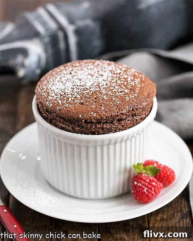 Elegantly presented individual chocolate soufflés in white ramekins, garnished with fresh raspberries, showcasing their perfect rise and golden-brown top.