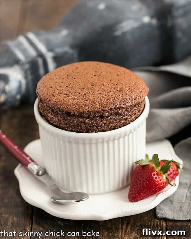A duo of individual chocolate soufflés presented in white ramekins, elegantly garnished with fresh strawberries, highlighting their fluffy texture.