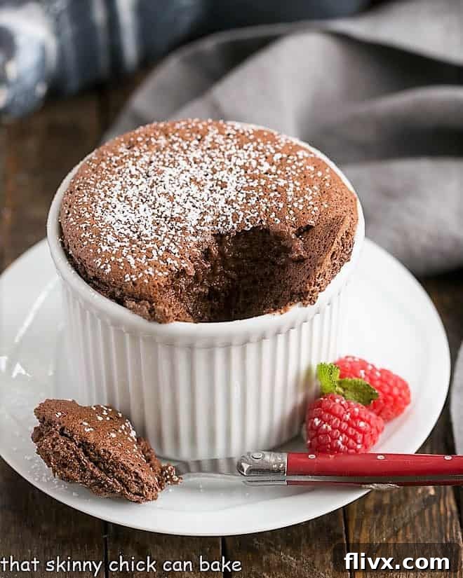 An individual chocolate soufflé in a white ramekin, with a spoonful removed to reveal its warm, airy interior and rich chocolate core.