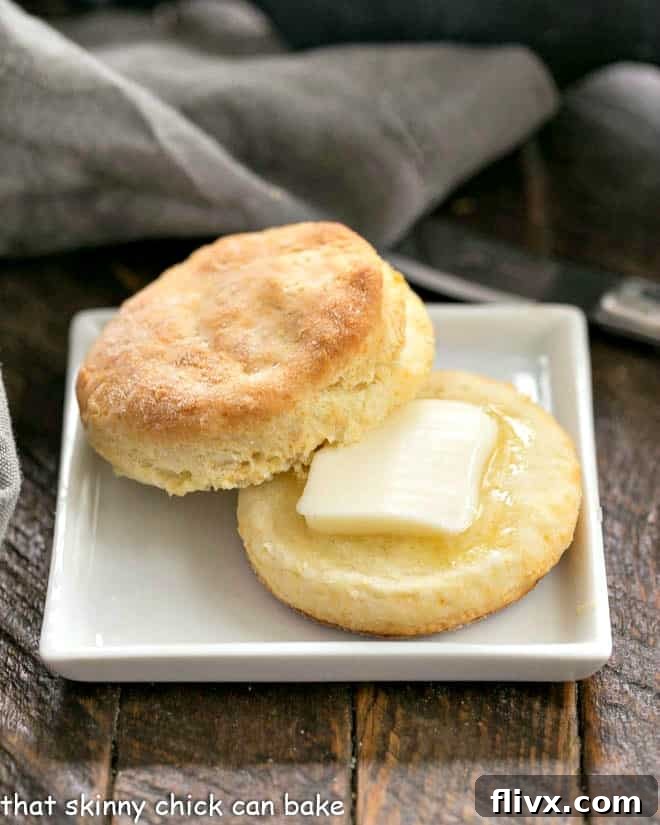 A perfectly split buttermilk biscuit with a pat of melting butter nestled inside, presented on a square white plate.