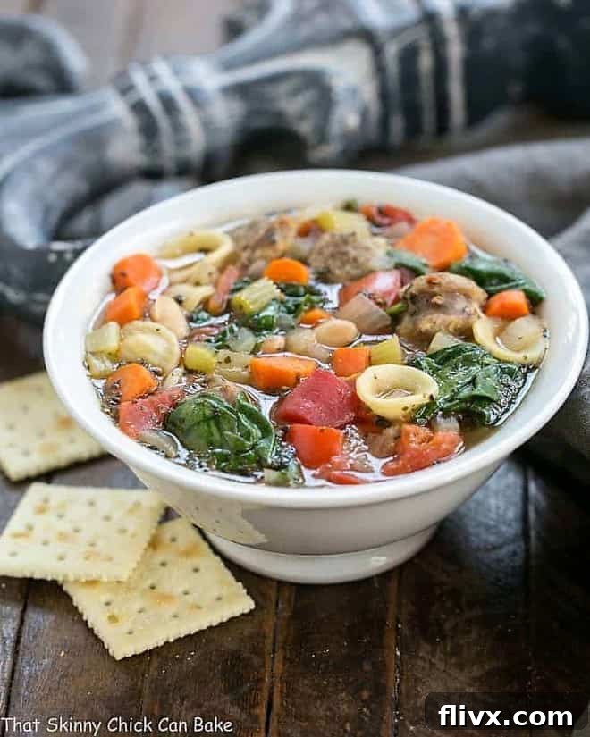 A steaming bowl of comforting Italian Sausage and Pasta Soup, garnished with fresh herbs and served with saltine crackers on the side, perfect for a cold winter night.