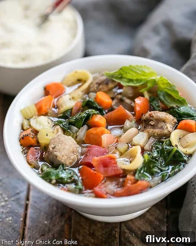 A close-up of Italian Sausage and Pasta Soup served in a rustic white bowl, with a small bowl of grated Parmesan cheese in the background, ready for topping.