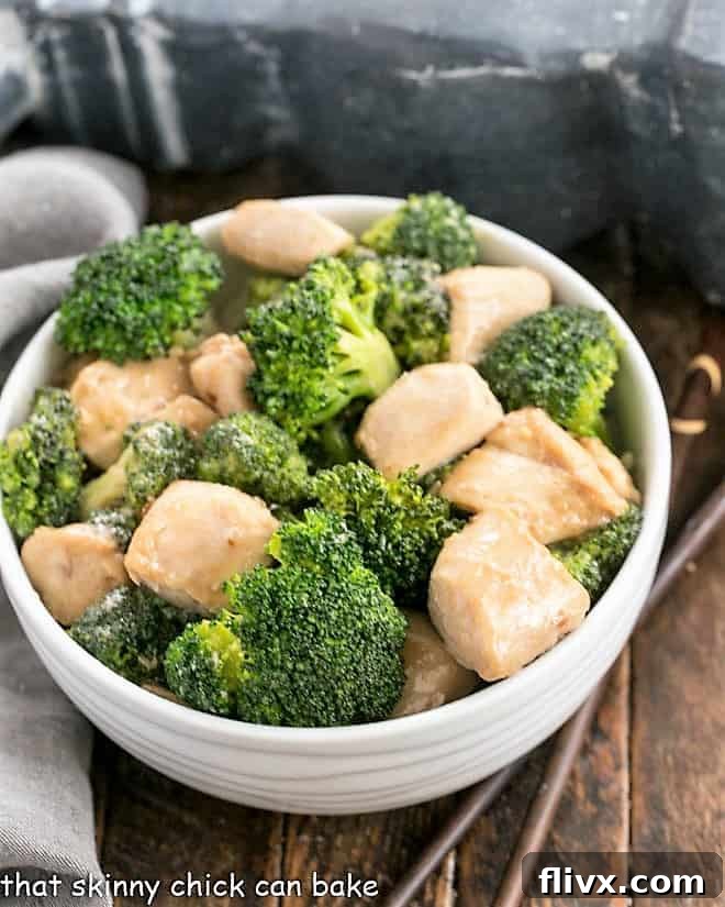 Overhead view of chicken and broccoli stir fry in a white ceramic bowl, garnished with sesame seeds.