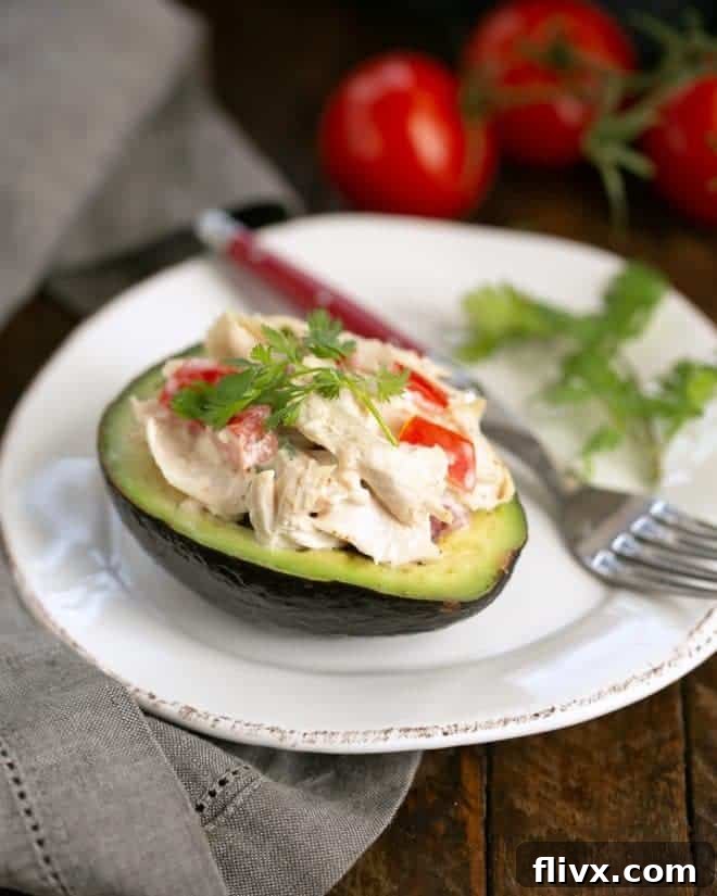 Easy Keto Southwestern Chicken Stuffed Avocados - A Quick & Healthy Low-Carb Dinner Idea A perfectly halved Southwestern Chicken Stuffed Avocado on a pristine white plate, garnished with fresh cilantro and a red-handled fork for serving.