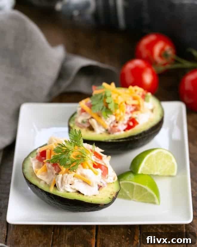 Southwestern Chicken Stuffed Avocados - Healthy, Flavorful & Gluten-Free Dinner Two vibrant Southwestern Chicken Stuffed Avocados halves, artfully arranged on a square white plate, accompanied by fresh lime wedges for an extra burst of citrus.