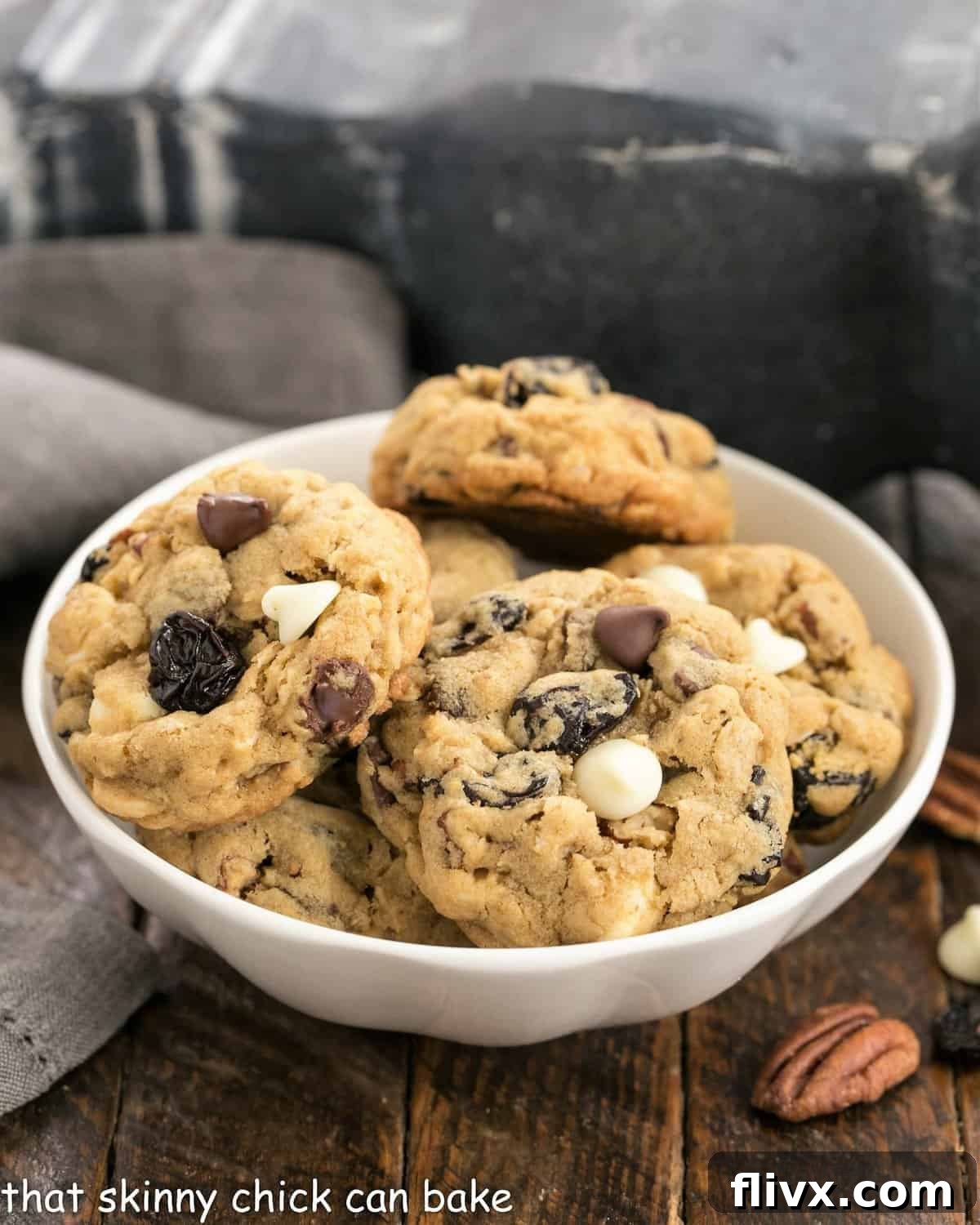Irresistibly chewy oatmeal cookies with dark and white chocolate chunks, toasted pecans, and dried cherries, artfully arranged in a small white ceramic bowl.