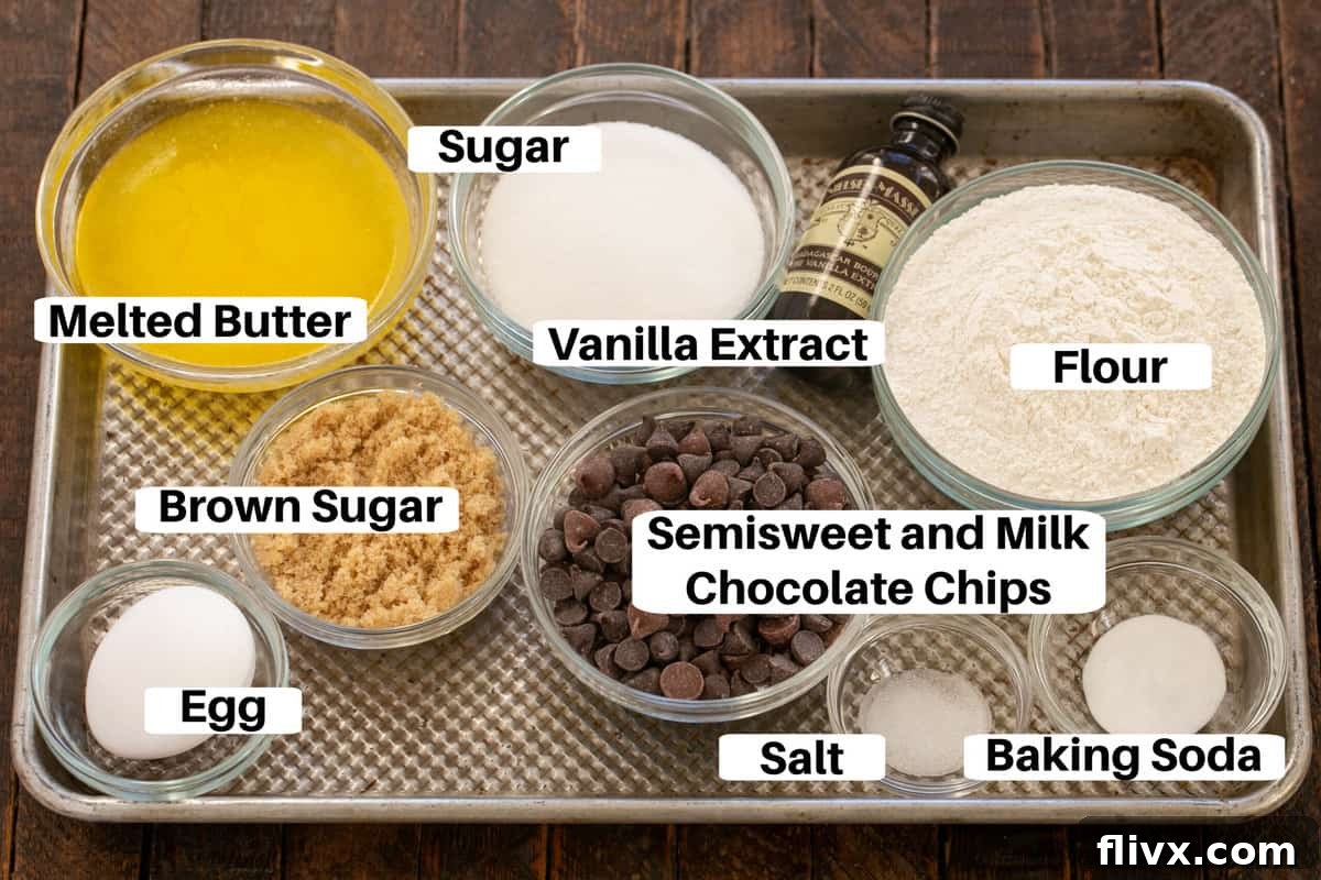 A meticulously arranged assortment of cookie ingredients, including butter, sugars, eggs, flour, chocolate chips, and leavening agents, neatly labeled on a metal sheet pan, ready for baking.