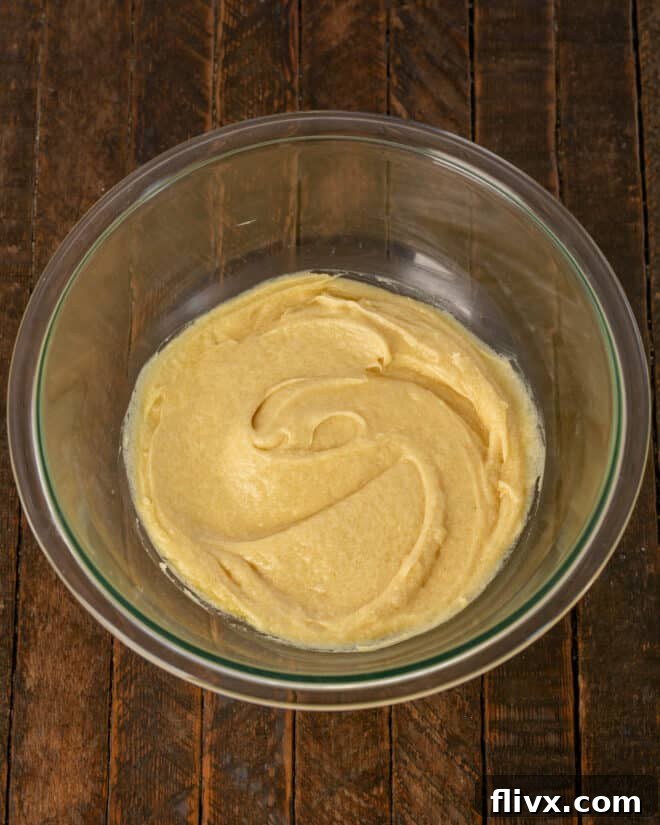 Step 1: Melted butter being mixed with both granulated and brown sugars, then vanilla and an egg are added, creating a smooth, creamy base for the cookie dough.