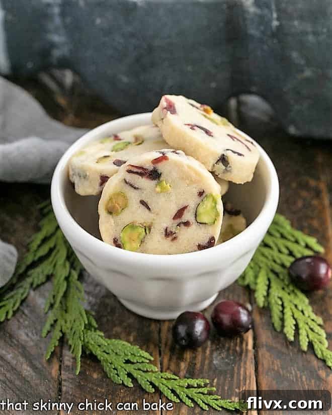Festive holiday shortbread cookies with red cranberries and green pistachios in a white bowl, ready to be enjoyed.