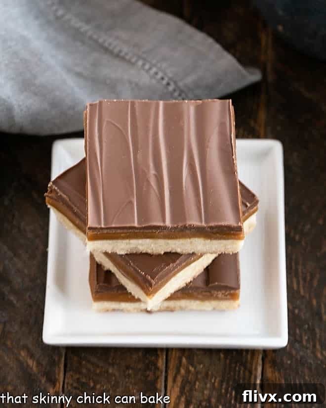 Overhead view of 3 homemade Twix bars stacked on a small square white plate, showcasing the three distinct layers: shortbread, caramel, and chocolate.