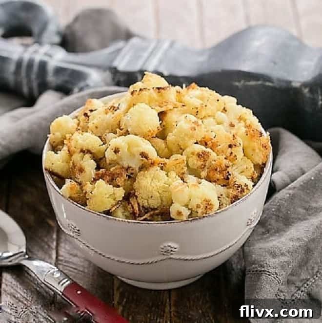 Roasted cauliflower with Parmesan and breadcrumbs in a white ceramic bowl with a red handled serving spoon. Golden brown and perfectly tender.