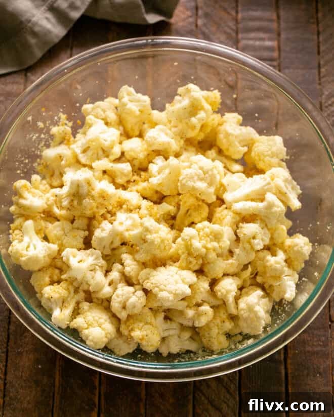 Bowl of cauliflower tossed with olive oil, ready for seasoning.
