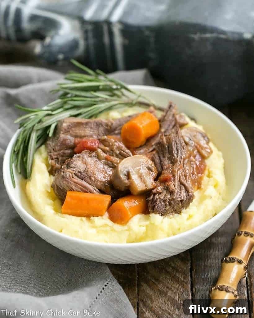 A hearty bowl of Oven Pot Roast with Mushrooms, Tomatoes & Red Wine, served alongside fluffy mashed potatoes, highlighting the rich sauce and tender beef.