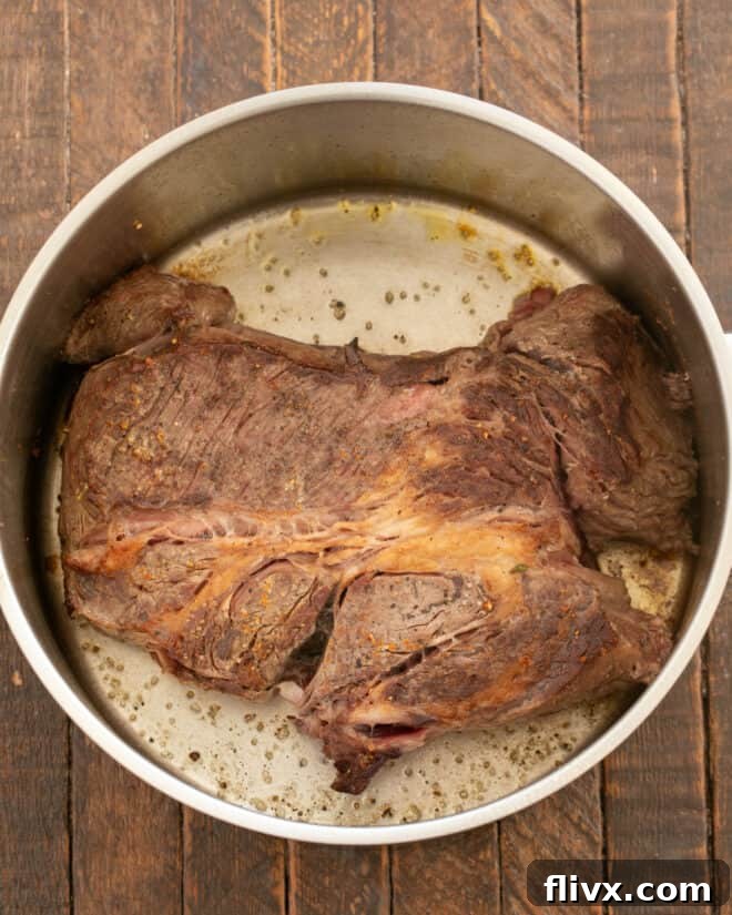 Step 1: Browning a chuck roast in a Dutch oven with olive oil until a rich crust forms.