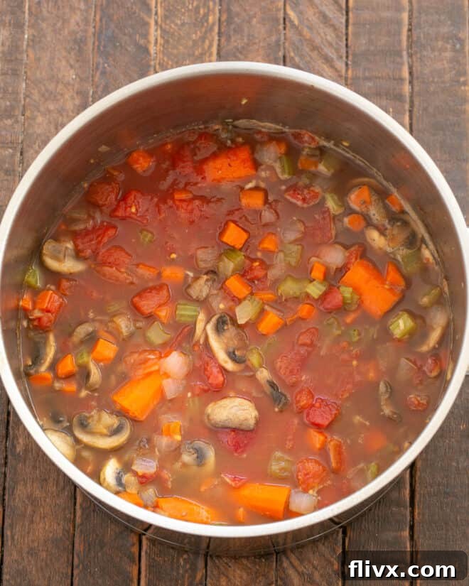 Step 4: Pouring chicken broth, dry red wine, and diced tomatoes with juice into the Dutch oven with the sautéed vegetables.