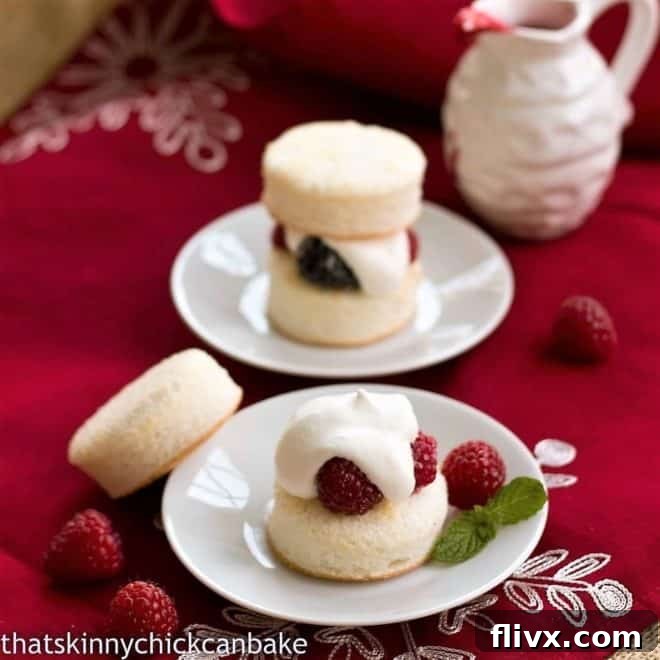 Two plates of Emeril's Angel Cake Sandwiches; one plate displays a fully stacked sandwich with a top cake round, while the other shows the top cake round delicately placed beside the berry and cream-filled base, highlighting the vibrant interior.