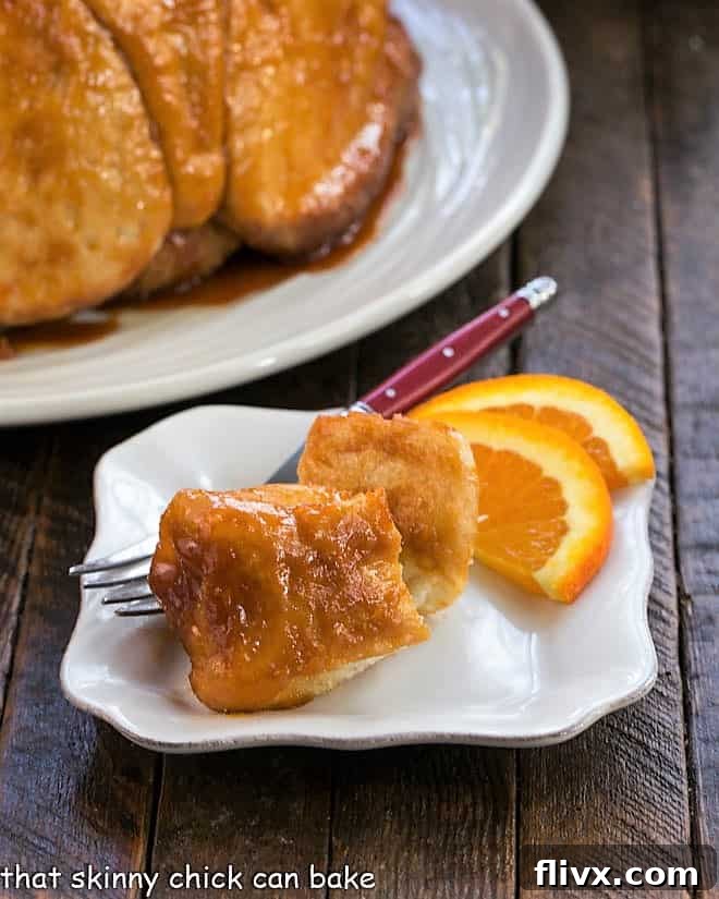Golden-brown, sticky-sweet Easy Monkey Bread pieces arranged on a small white plate, garnished with fresh orange slices, highlighting its delectable texture and inviting presentation.
