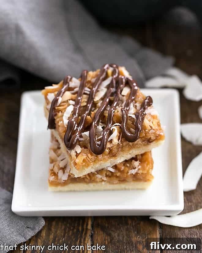 Homemade samoa bars stacked high on a pristine white plate, showcasing their layers of golden shortbread, gooey caramel, toasted coconut, and elegant chocolate drizzle.