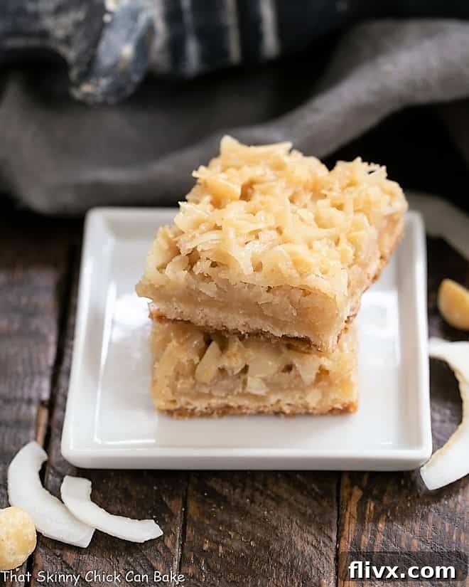 Coconut Macadamia Nut Bars stacked elegantly on a square white plate, showcasing their inviting texture and golden-brown topping.