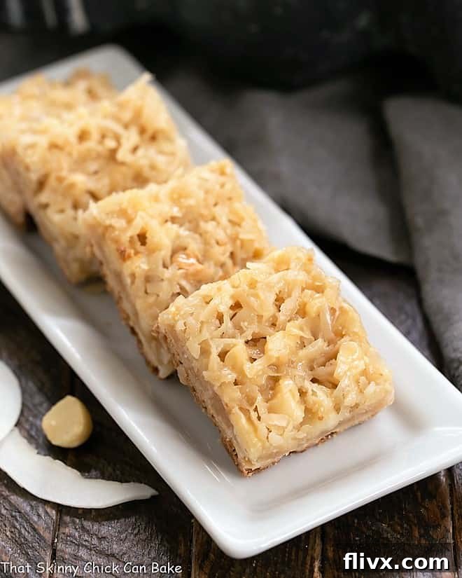 Several Coconut Macadamia Nut Bars arranged neatly on a elegant white ceramic tray, highlighting their golden crust and texture.