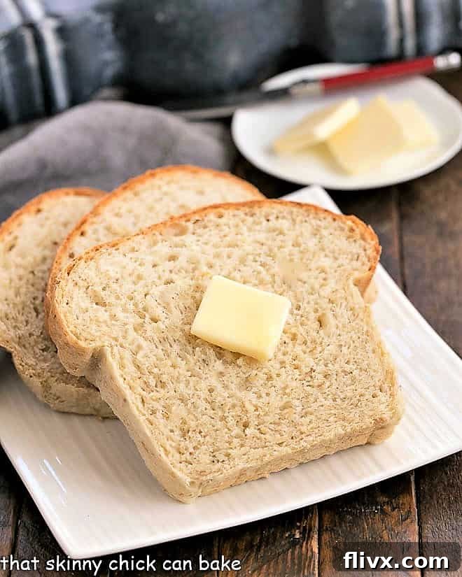 Three slices of oatmeal bread on a square plate with the top slice with a pat of butter